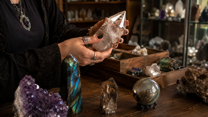 Person carefully inspecting a clear quartz specimen by hand among mineral displays in a crystal shop.