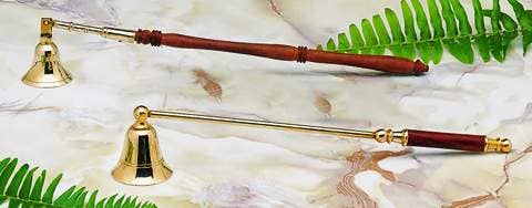 Two brass candle snuffers with wooden handles on a marble surface with green leaves.