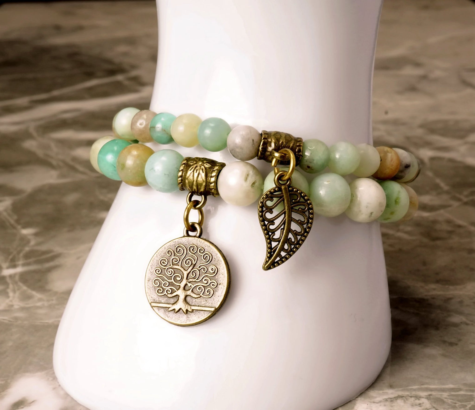A two-piece bracelet set with one featuring leaf and tree of life charms, and the other with a mix of blue and green beads.