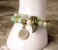A two-piece bracelet set with one featuring leaf and tree of life charms, and the other with a mix of blue and green beads.