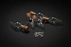 Glass bottles with cork stoppers and small metal hooks on a dark fabric background