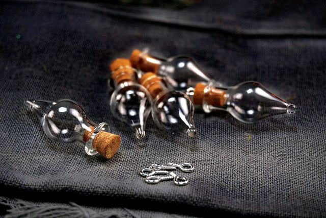 Glass bottles with cork stoppers and small metal hooks on a dark fabric background