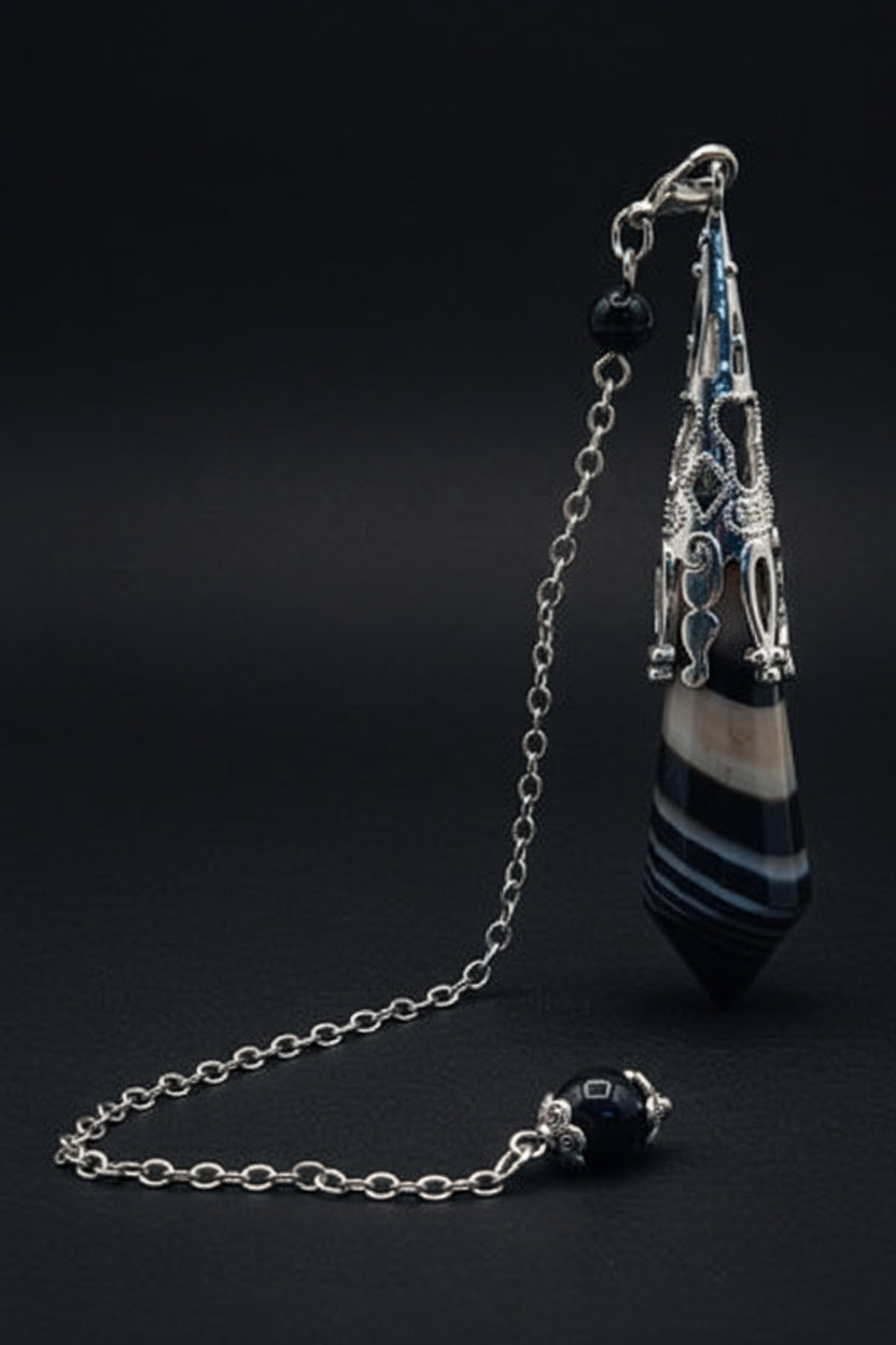 Sardonyx pendulum displayed on a white surface with greenery