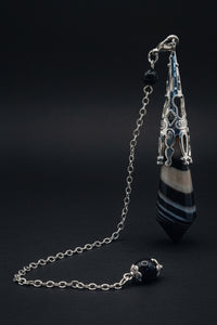 Pendulum with a blue pendant on a white surface with greenery