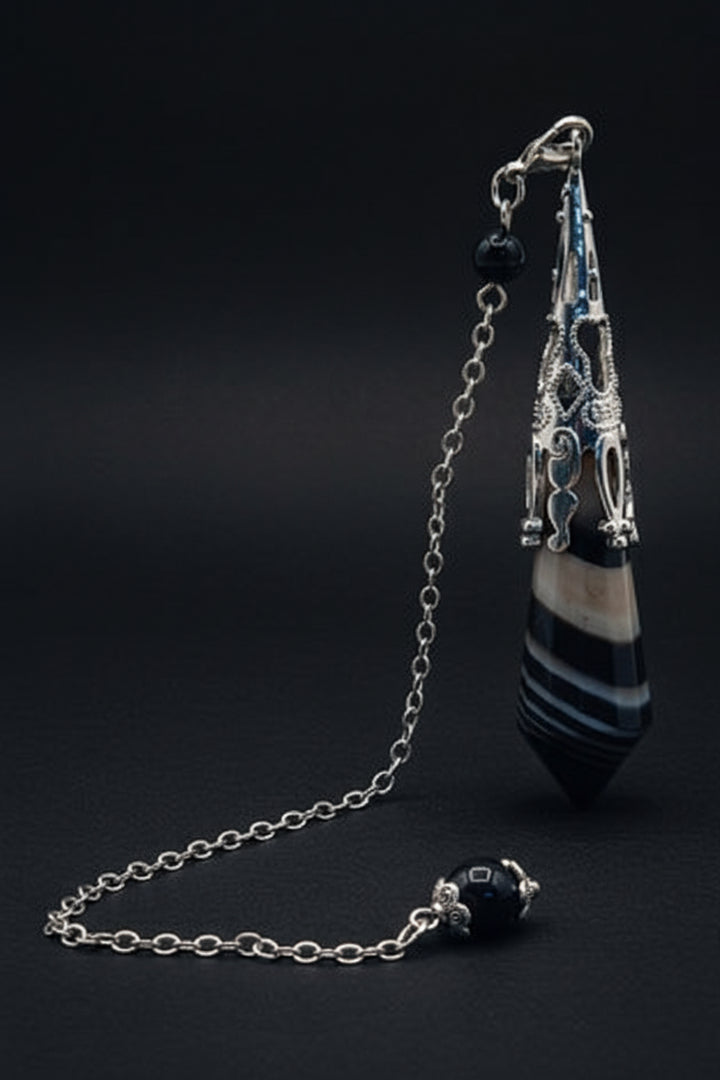 Sardonyx pendulum displayed on a white surface with greenery
