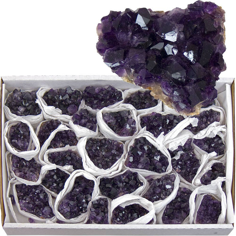 Box of amethyst crystals with a large amethyst geode on top