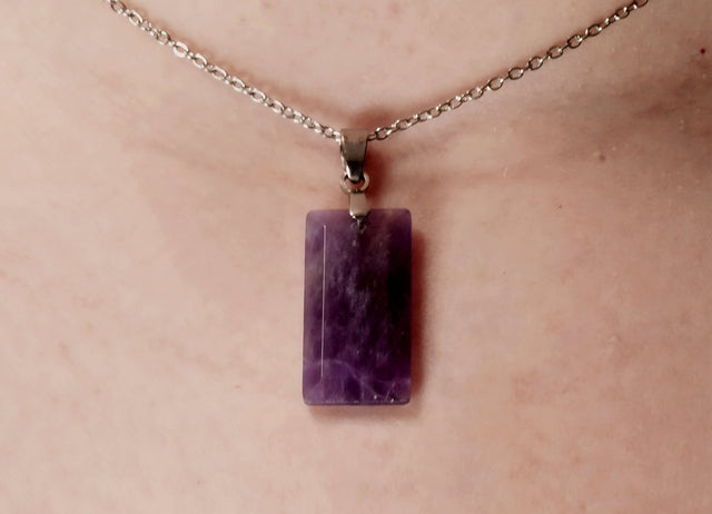 An amethyst faceted crystal pendant necklace displayed on a person's chest.