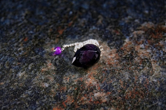 Silver ring with purple gemstone on a textured stone surface.