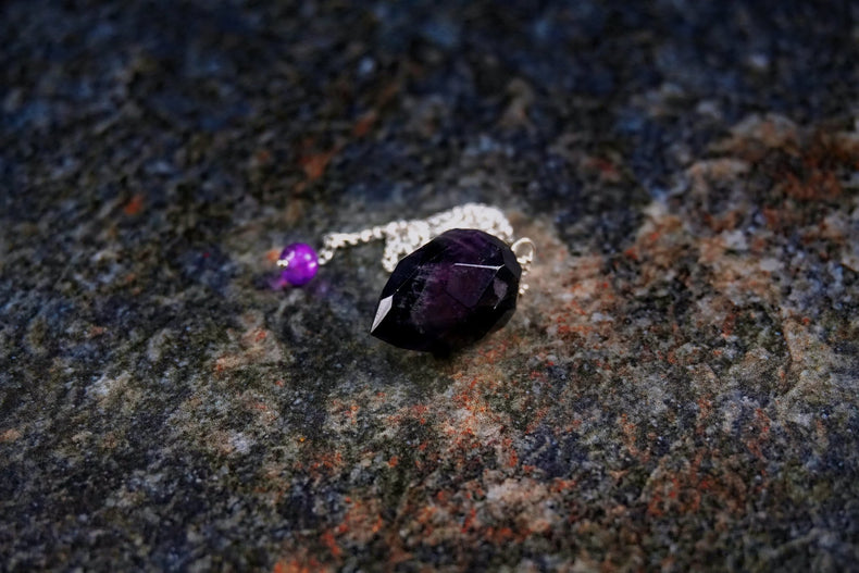 Silver ring with purple gemstone on a textured stone surface.