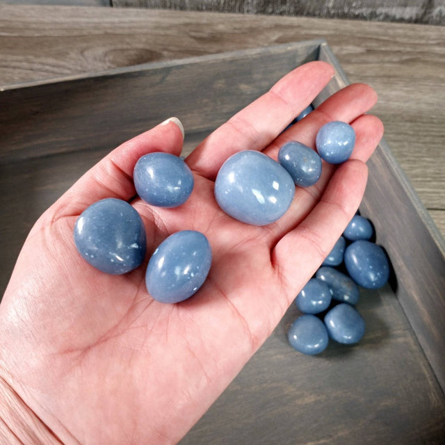 Hand holding blue stones with a wooden tray in the background