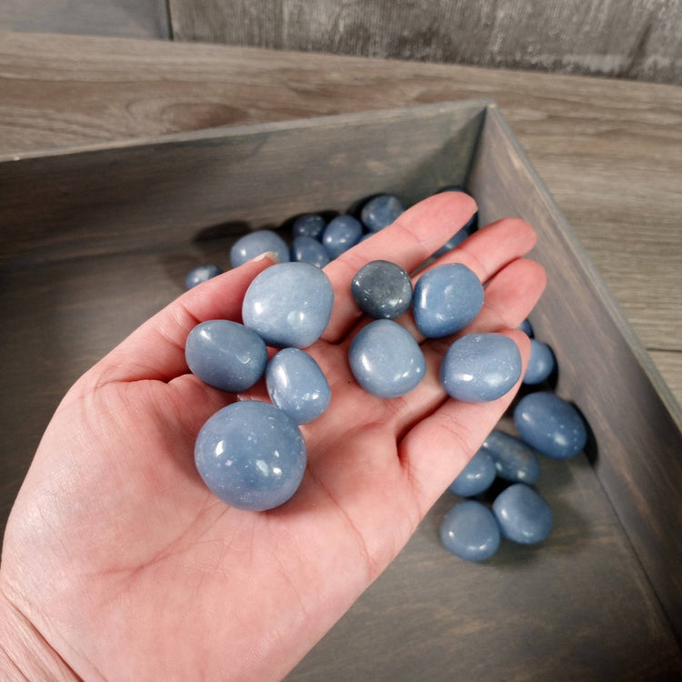 Hand holding blue stones with a wooden tray in the background