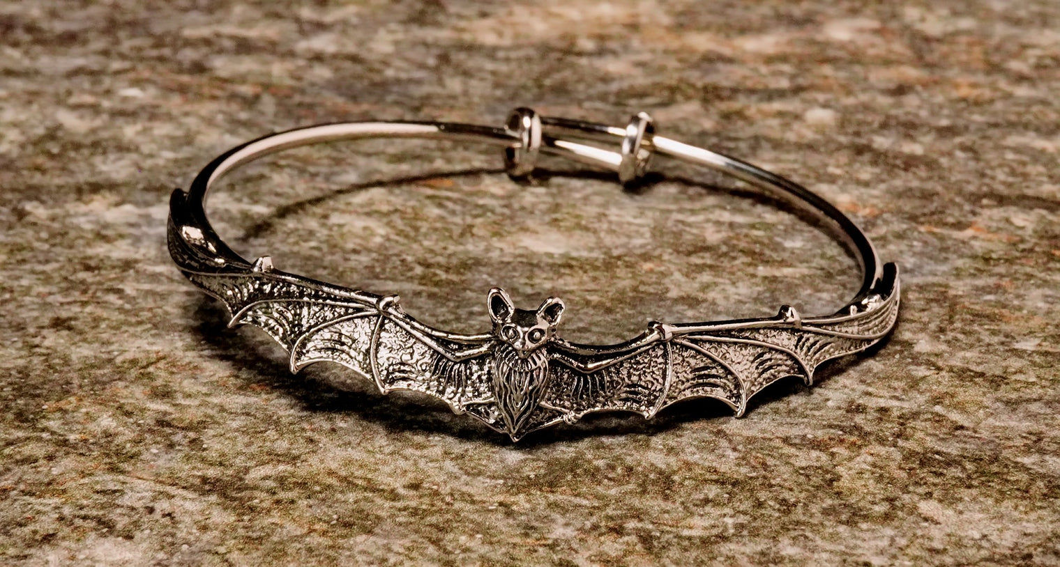 A metal bangle bracelet designed with a bat motif, featuring a silver finish.
