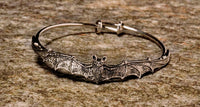 A metal bangle bracelet designed with a bat motif, featuring a silver finish.