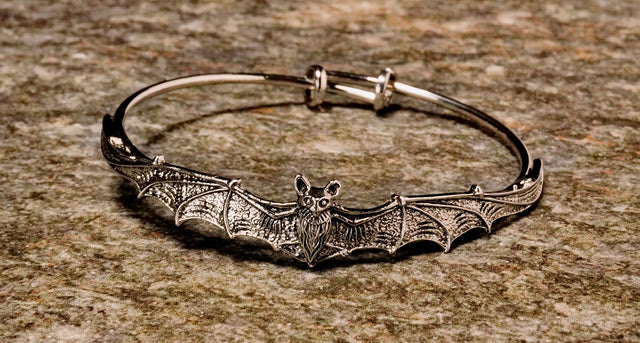 A metal bangle bracelet designed with a bat motif, featuring a silver finish.