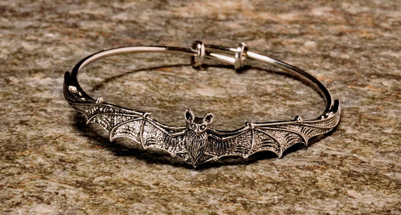A metal bangle bracelet designed with a bat motif, featuring a silver finish.