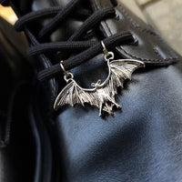 Silver-tone bat boot charm attached across black boot laces