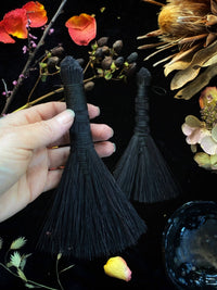 Black tassels held by a hand with flowers and leaves in the background