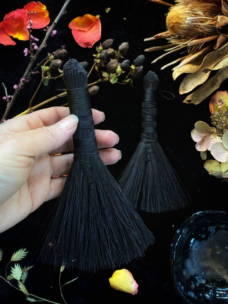 Black tassels held by a hand with flowers and leaves in the background