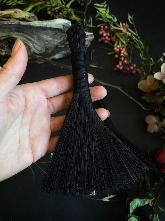 Black tassel held by a hand with a dark background and decorative elements.