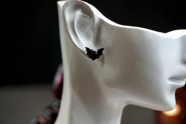 White ceramic sculpture of a face with a black bat earring on a dark background