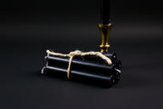 A small black chime candle tied with a string to a metal holder, set on a stone surface with a gold-colored handle.