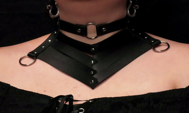 A close-up image of a person wearing a black leather choker collar with five bands and three metal rings.