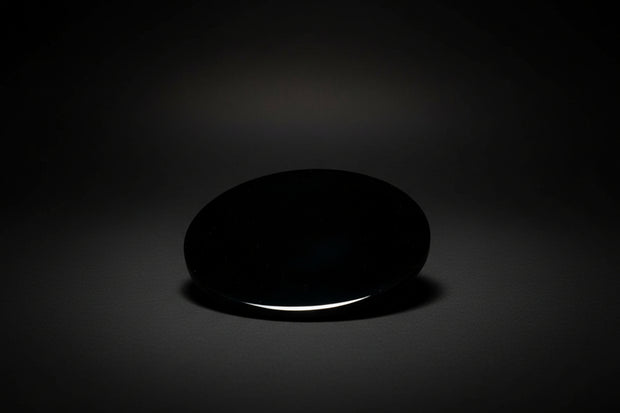 Hand holding a round polished dark mirror sold as black obsidian