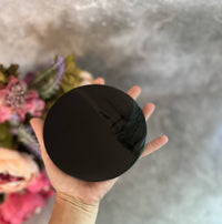 Hand holding a black round object against a blurred floral background