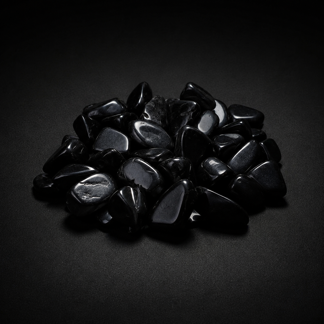 Pile of polished jet-black Obsidian tumbled stones with glossy reflections on a matte black surface