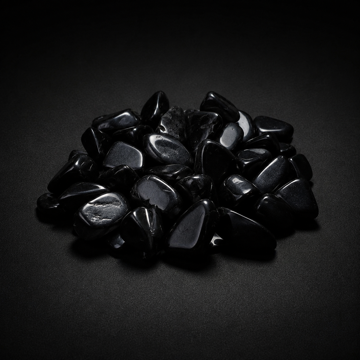 Pile of polished jet-black Obsidian tumbled stones with glossy reflections on a matte black surface