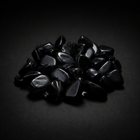 Pile of polished jet-black Obsidian tumbled stones with glossy reflections on a matte black surface