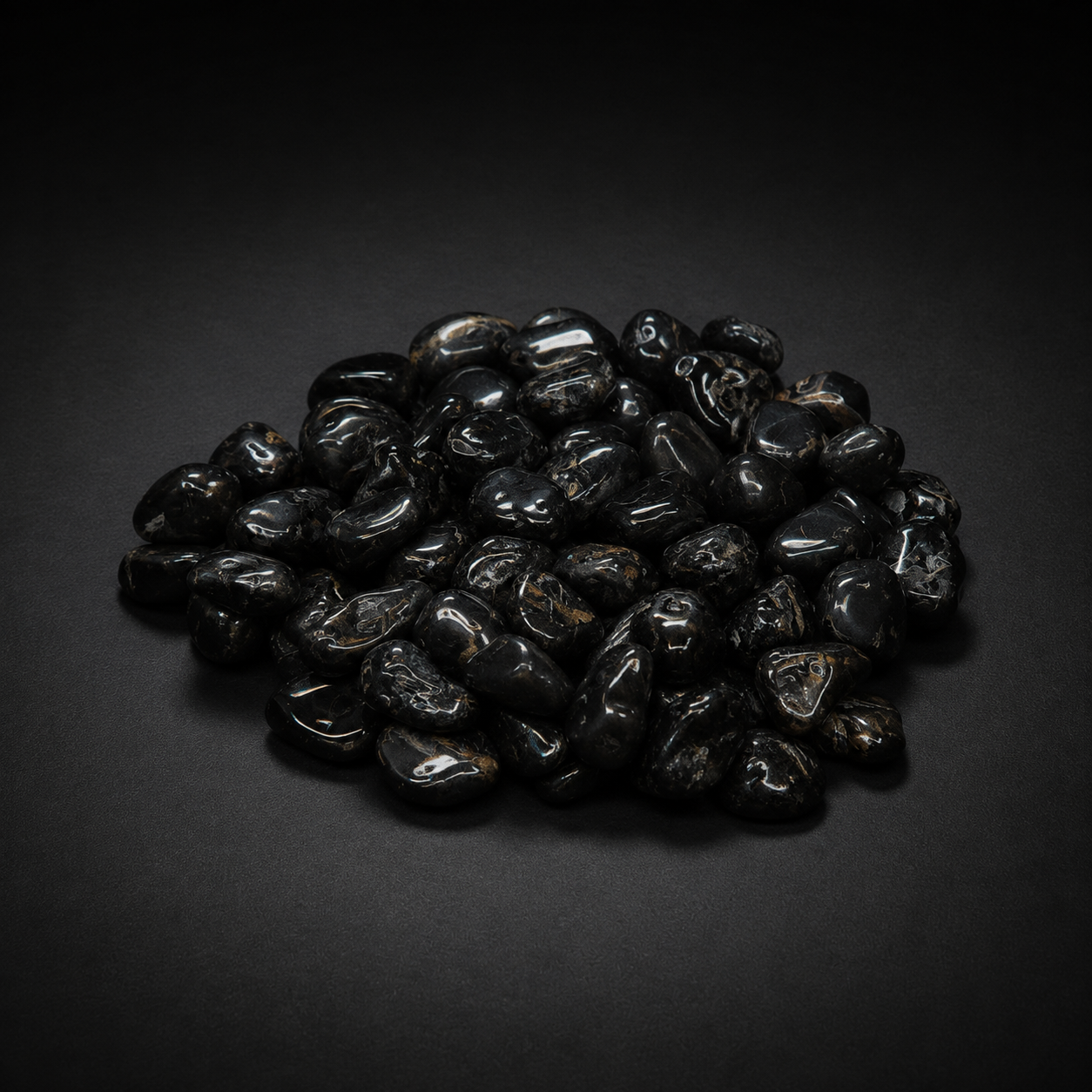 Pile of polished black stones sold as Black Onyx with subtle natural markings on a matte black surface
