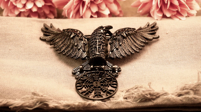 A metal hair clip in the shape of a black raven with outstretched wings, featuring the Helm of Awe symbol etched on its body.