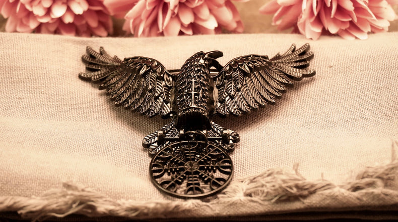 A metal hair clip in the shape of a black raven with outstretched wings, featuring the Helm of Awe symbol etched on its body.