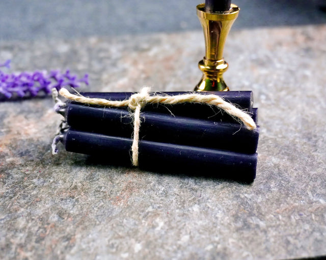 A small black chime candle tied with a string to a metal holder, set on a stone surface with a gold-colored handle.