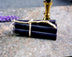 A small black chime candle tied with a string to a metal holder, set on a stone surface with a gold-colored handle.