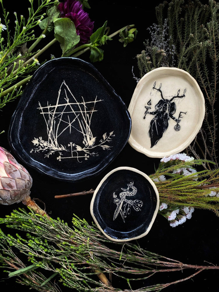Three decorative plates with intricate designs on a dark background with greenery.