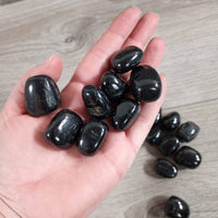 Hand holding shiny black stones on a wooden surface