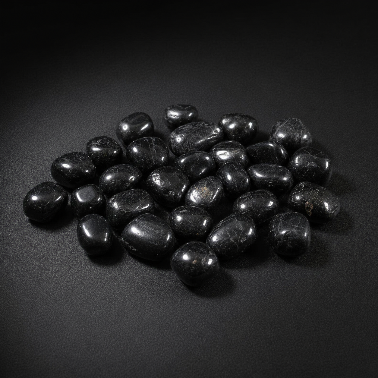 Polished Black Tourmaline tumbled stones with subtle natural inclusions on a matte black surface