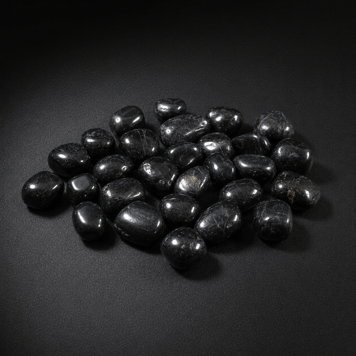 Polished Black Tourmaline tumbled stones with subtle natural inclusions on a matte black surface