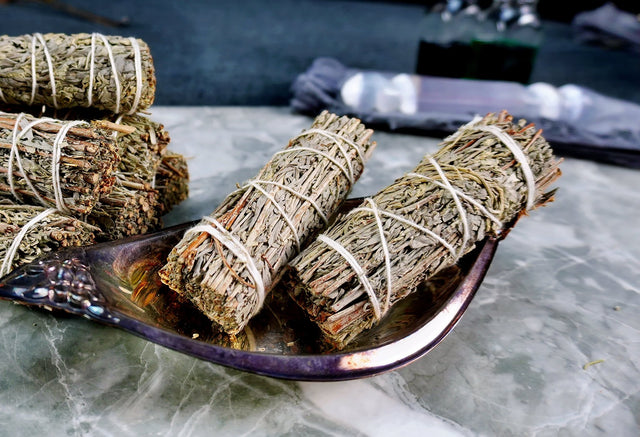 Bundles of Blue Sage Smudge Sticks tied with string, placed on a metal dish on a marble surface.