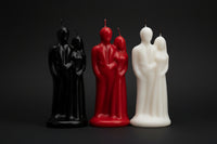 Three candles shaped like people, one black, one red, and one white, on a white background.
