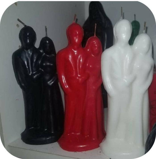 Three candles shaped like people, one black, one red, and one white, on a white background.