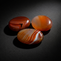 Three polished orange-red carnelian palm stones with natural banding on a matte black surface