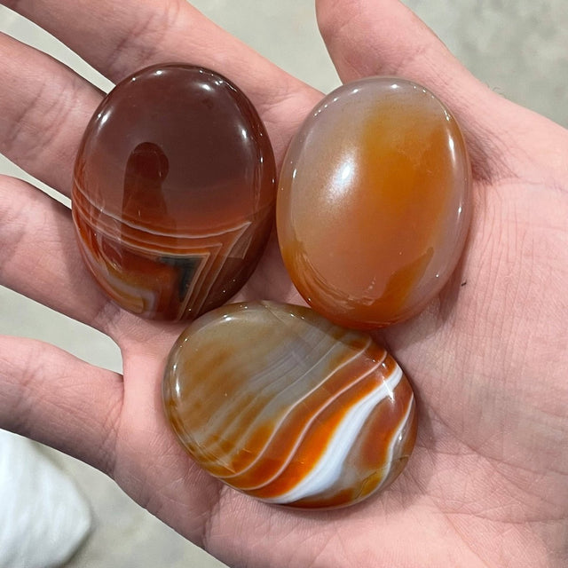 Three marbled agate stones held in a hand against a neutral background