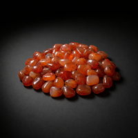 Pile of polished translucent orange-red Carnelian tumbled stones on a matte black surface