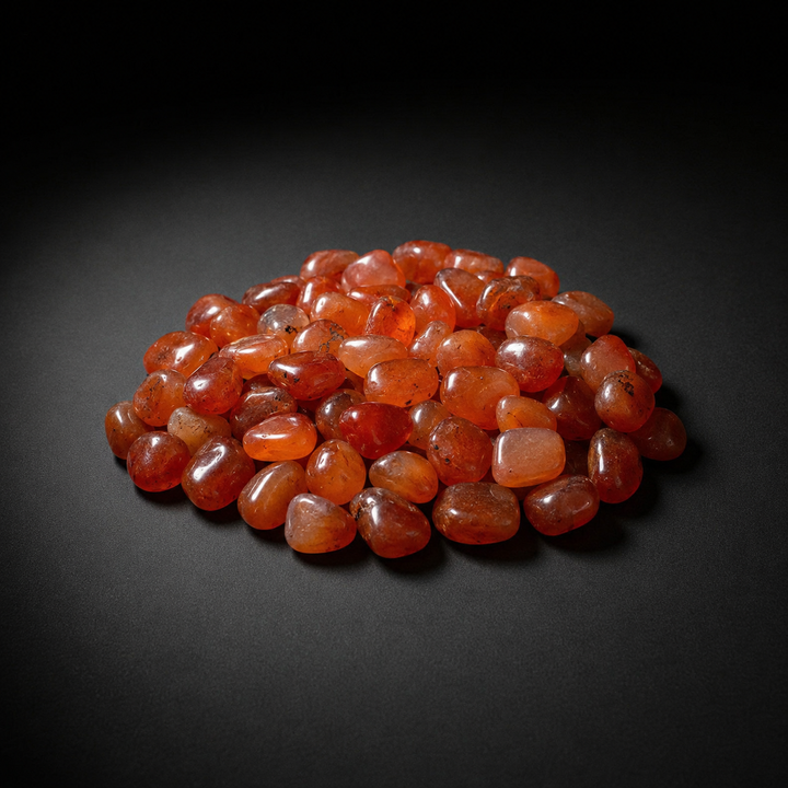 Pile of polished translucent orange-red Carnelian tumbled stones on a matte black surface