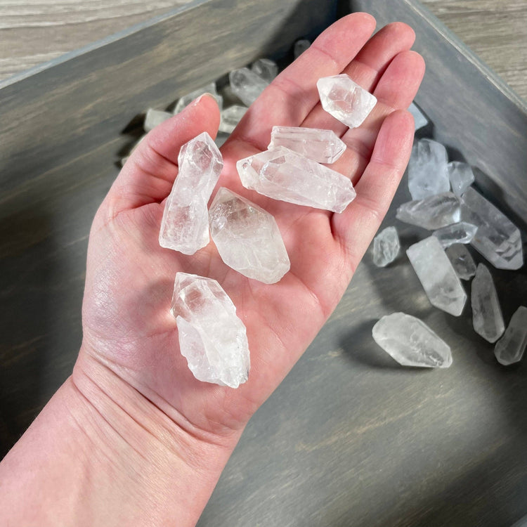 Hand holding clear crystal stones with a tray of additional stones below on a wooden surface.