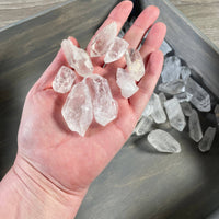 Hand holding clear crystal rocks with a tray of additional crystals in the background.