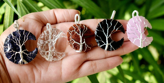 Hand holding five moon-shaped jewelry pieces against a natural background